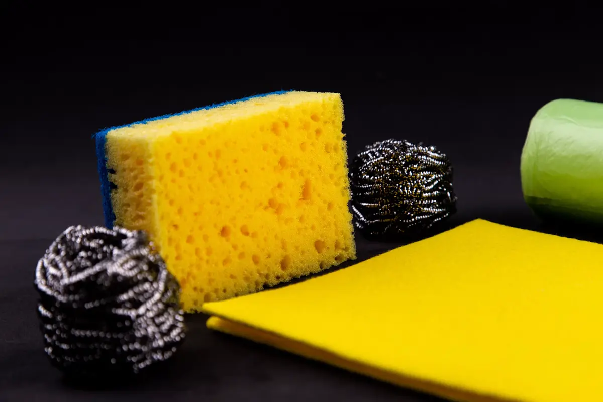 A sponge, steel wool scouring pads, and cleaning cloths arranged together