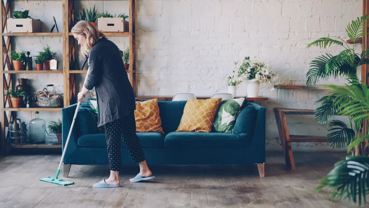 Person mopping a wood floor in a plant-filled living room