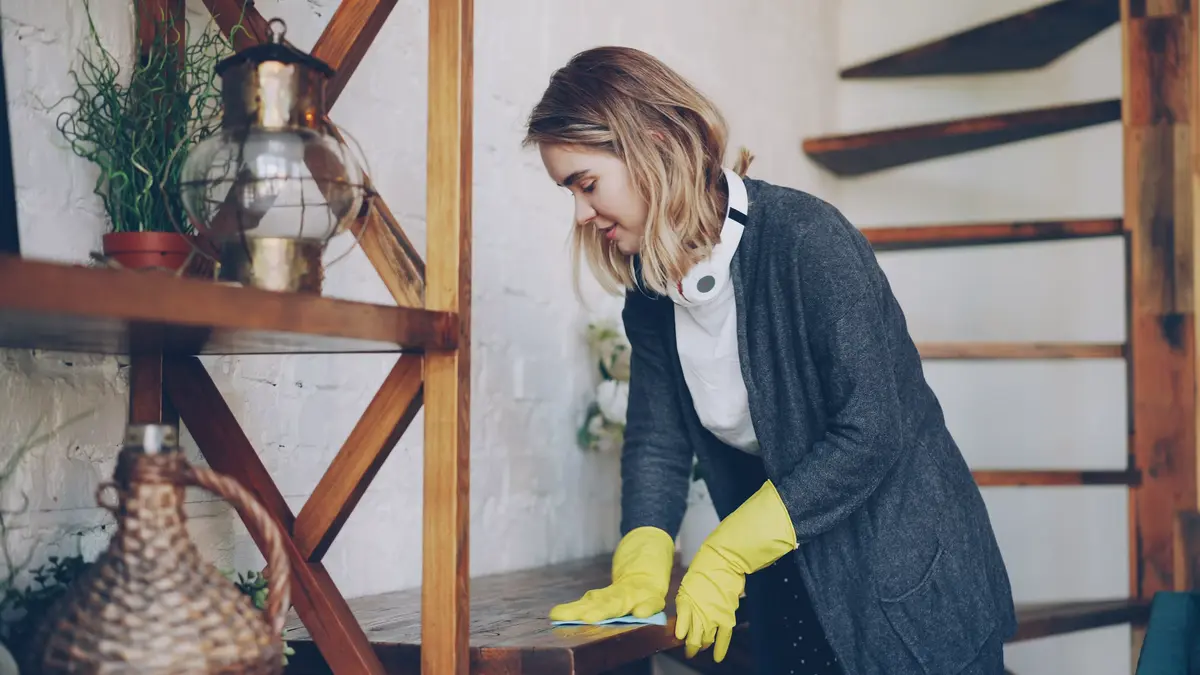 Person wearing rubber gloves wiping down a wooden shelf